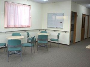 センター内の部屋の画像。白い丸テーブルが2つとその周りに緑に椅子が数脚ずつ置かれている。